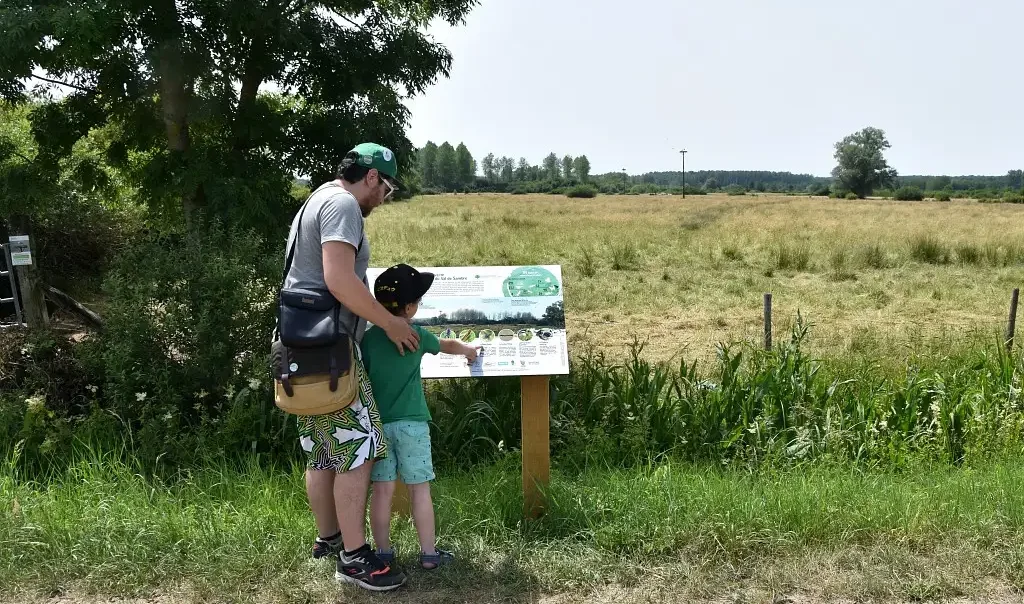 Photographie d'un promeneur et de son enfant devant une table de lecture de la Réserve naturelle régionale des Prairies du Val de Sambre ( Nord)